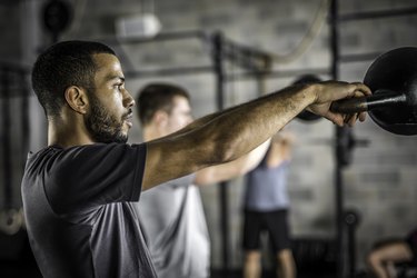 两个男人摆动kettlebells在健身房