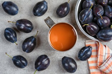 Ripe plums and plum juice in a mug on the table.