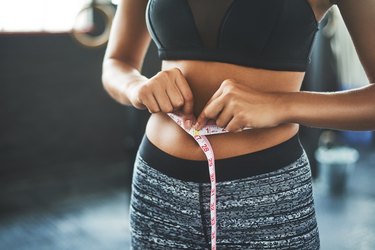 Close view of an athletic woman measuring her waist with a tape measure to calculate her body fat percentage