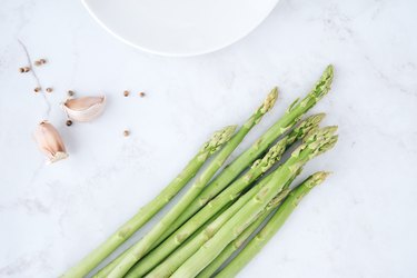 Fresh green asparagus with garlic and white peppercorns on marble table