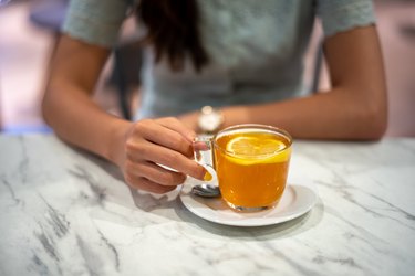Young asian woman's hand holding a cup of hot lemon tea on top of marble table