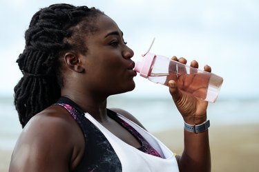 Black woman wearing workout clothes and drinking water