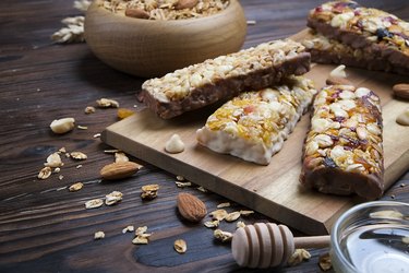 A trail mix bowl of dried fruit, raisins, cranberry with almonds, raisins, seeds, cashew, hazelnut nuts with honey. Vegetarian fitness energy bar snacks. Close up, top side view, background.