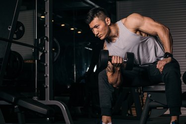 Asian man doing concentration curl with dumbbell for bicep workout for mass