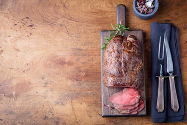 Roast beef on cutting board. Wooden background. Top view. Copy space.