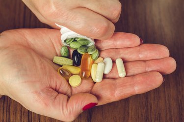 a person's hands with painted nails pouring a mixture of vitamin pills out of a white bottle