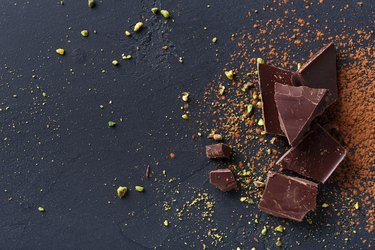Broken chocolate pieces and cocoa powder on black background