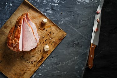 Delicious smoked ham on a wooden board, on a dark concrete background with spices. Top view