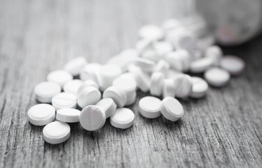 Handful of small white pills on a wooden table.