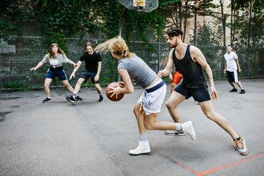 Woman playing basketball in a park preparing to pass the ball to another player.