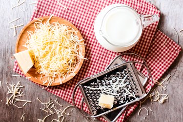 Ingredients for pasta dish or pizza - milk, freshly grated parmesan cheese on a wooden table, and kitchen utensils (grater) on a wooden table, top view. Messy style. Preparations for cooking process.