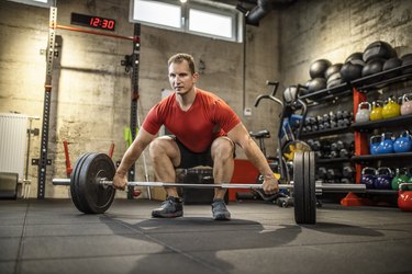 Mature strong man lifting weights at cross training in gym. Bodybuilder doing squatting with a barbell.