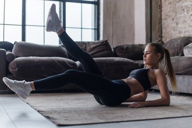 Young sporty female doing abs workout in living room performing alternate leg raising and crunch exercise