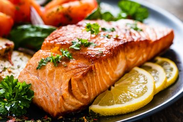 Barbecued salmon, fried potatoes and vegetables on wooden background