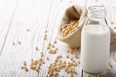 Non-dairy alternative Soy milk or yogurt in glass bottle on white wooden table with soybeans in hemp sack