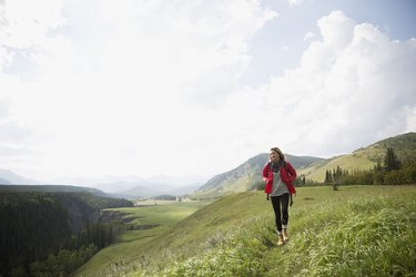Woman with backpack hiking in remote sunny rural field
