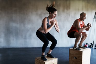 Two people in workout gear performing box jumps to train muscles in vertical jump in the gym.