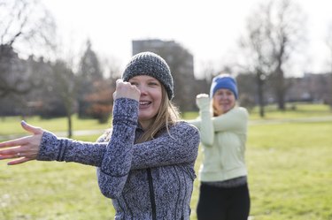 Smiling woman exercising, stretching arm in sunny park