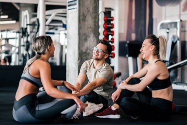 Happy friends sitting on the floor in the gym and talking.