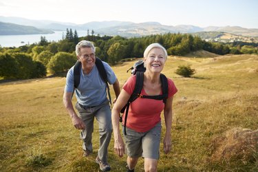 Portrait Of Senior Couple Climbing Hill On Hike Through Countryside In Lake District UK Together