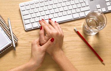 A woman sitting at a desk and massaging her swollen fingers