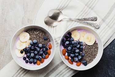 Two breakfast bowls with yogurt, berries, banana, almonds and chia seeds