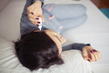 Woman using ear drops at home, as a natural remedy for earache