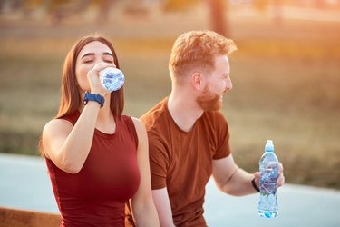 Couple making pause in an urban park during jogging or exercise drinking water