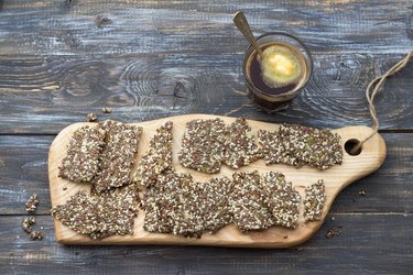 Delicious healthy multigrain gluten-free crackers, ketogenic, from chia seeds, flax, sesame and ground pumpkin seeds and keto coffee in glass with spoon of butter Ð¾n wooden table
