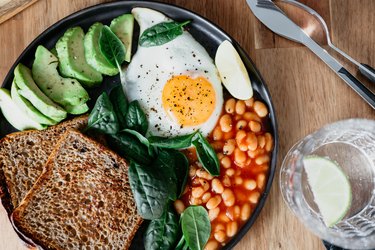 Healthy breakfast or lunch at home or cafe with fried egg, avocado, toasts, beans and fresh spinach on a wooden table.