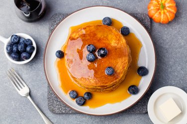 Pumpkin pancakes with maple syrup and blueberries on a plate.