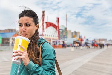 A woman drinking a large soda at the Coney Island boardwalk