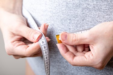 Close view of a person measuring waist with a tape measure