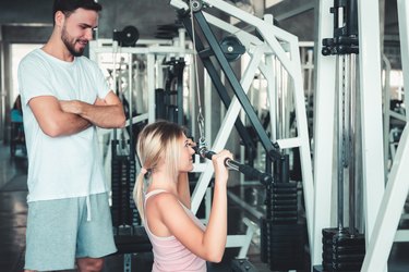 Portrait of Beautiful Woman is Exercised Training With Bodybuilder Machine in Fitness Club., Attractive of Sporty Girl Doing Working Out With Her Trainer in Gym, Healthy and Sport Lifestyle Concept.