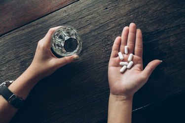 Cropped Hands Of Woman Holding Pills And Drinking Water In Glass