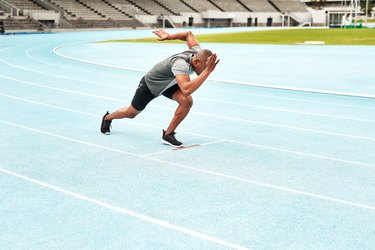 Black man sprinting outside on blue track