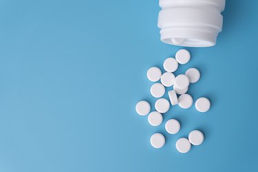 Small, white, round pills spilling out of a jar on a blue background.