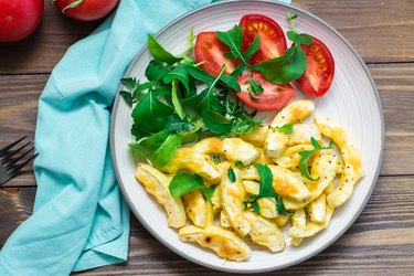 Slices of zucchini baked in spices with cheese on a plate with tomatoes and arugula on a wooden table