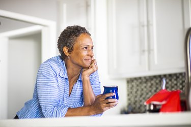 an older adult holds a blue coffee mug and smiles in a white kitchen