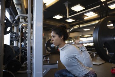 Focused woman doing barbell squats in gym