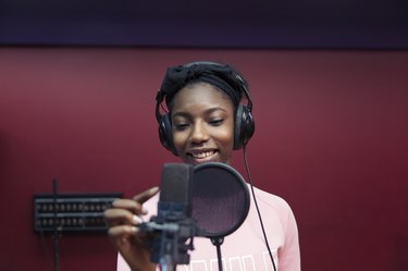 Smiling teenage girl musician recording music, singing in sound booth