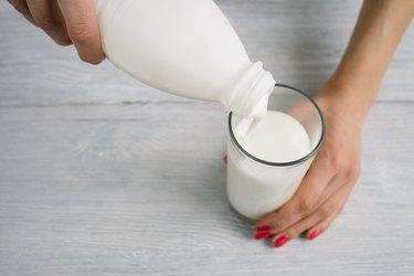 Female hands with red manicure pouring milk