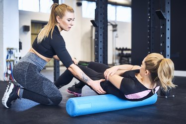 Woman massages muscles with personal trainer after gym workout