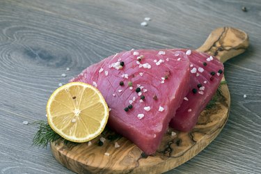 Raw tuna fillet with dill, lemon and peppers in olive cutting board