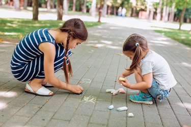 Two girls sitting and drawing with chalk on asphalt in park at normal heights and weights