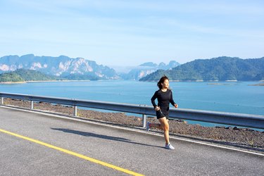 Asian woman running on road with mountain and lake background