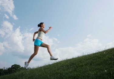 person in shorts and a tank top running up a steep grassy hill