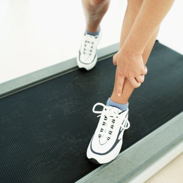 feet on treadmill wearing white workout sneakers with one hand grabbing shin