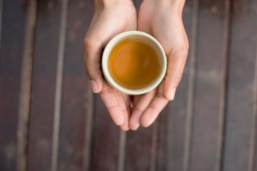 Top down photo of two hands cupped around a small cup of tea