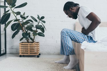 young african american man suffering from stomach ache while sitting on bed